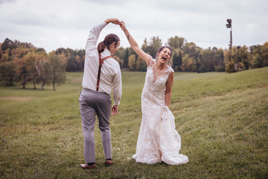 Wedding couple doing twirls in a field and laughing with each other