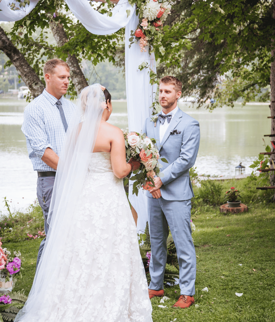 When thinking how to plan elopement considering a beautiful outdoor backdrop like this is gorgeous. Image of a couple standing near a lake during wedding ceremony. 