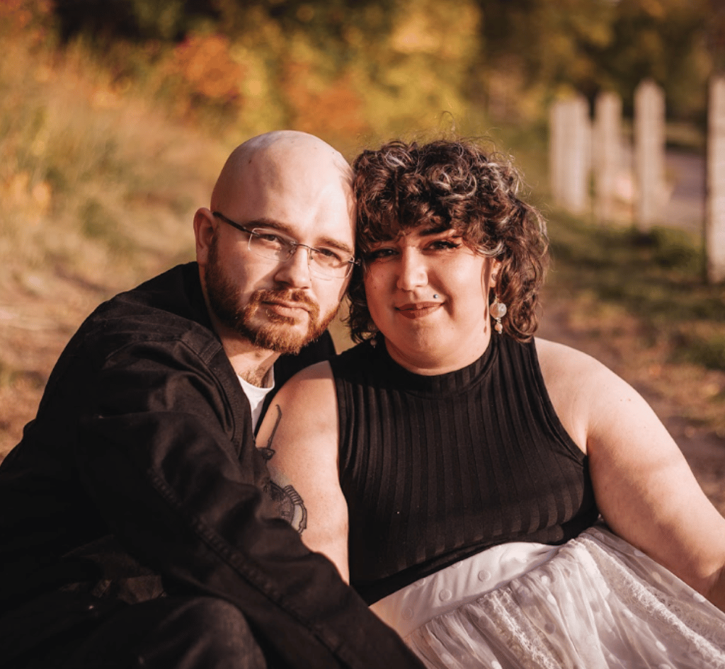 Image of a couple sitting on a dirt path facing the camera smiling for their engagement photos. 