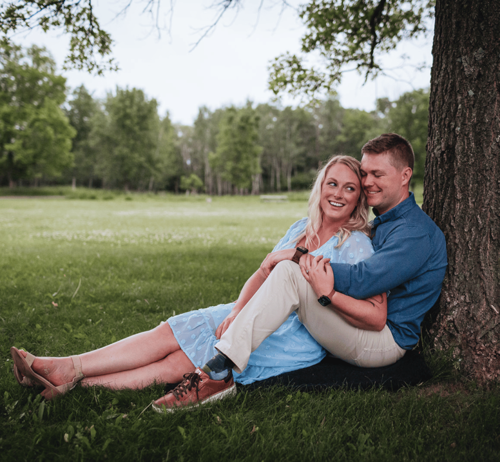 Woman and man are sitting under a tree laying entangled in each other. This is an example of an engagement photo sessions pose you can do!