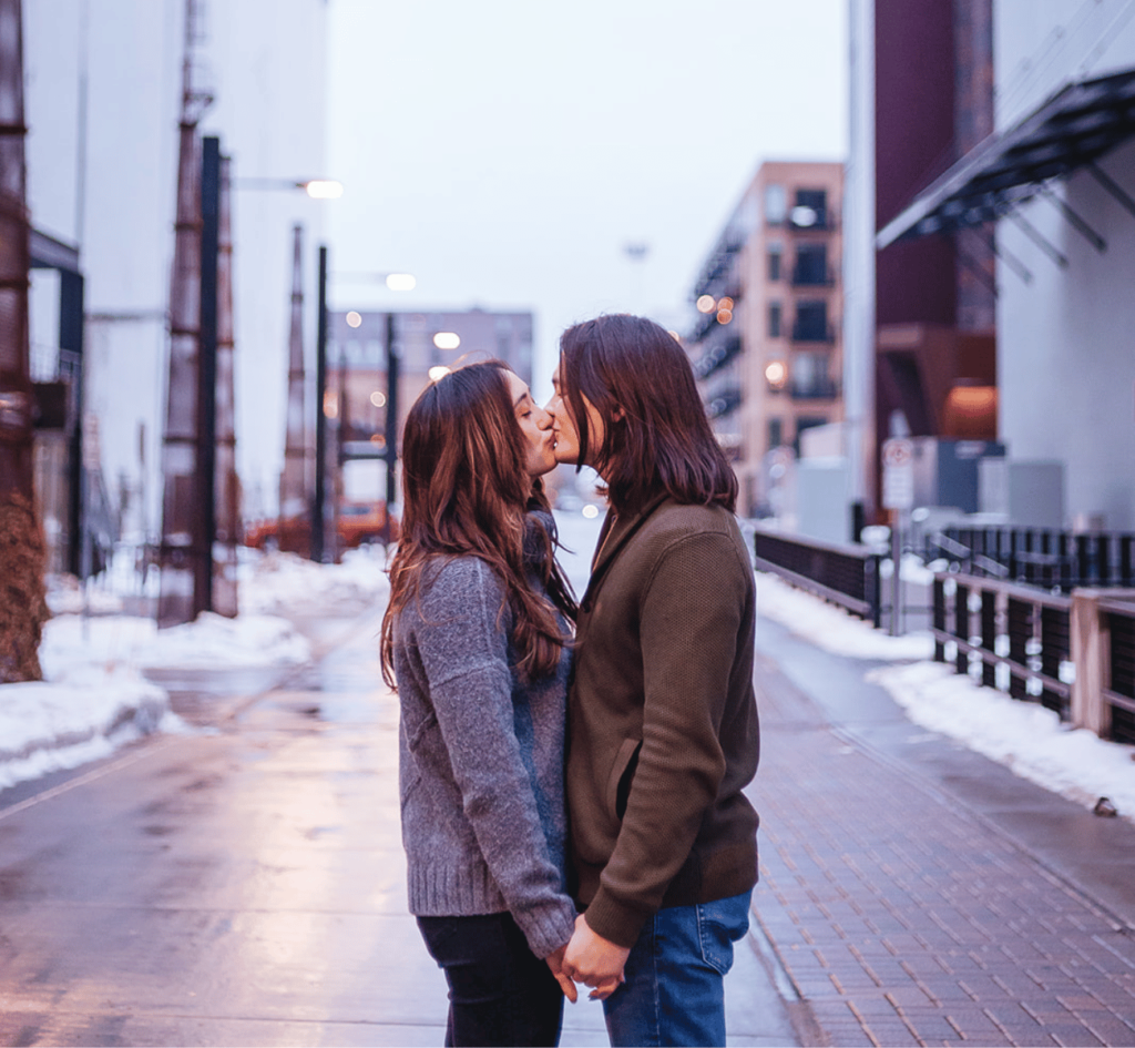 Image of a couple standing in the middle of a street kissing in the winter. 