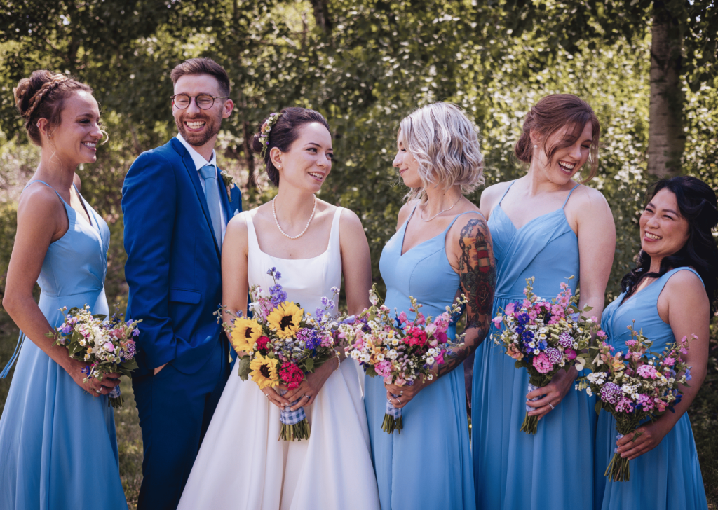 Image of a blushing bride with her wedding party in blue dresses and suit. This wedding took place at Elm Creek Park in Minneapolis. 