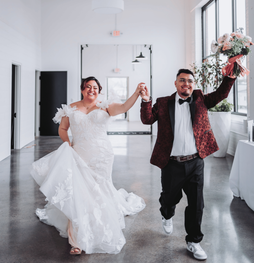 Image of a wedding couple with their arms raised in excitement after their wedding. 