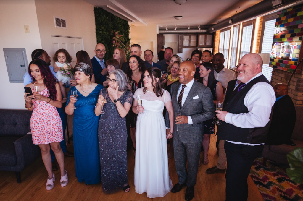 Image of a couple and all their wedding guests listening to speeches and smiling. 