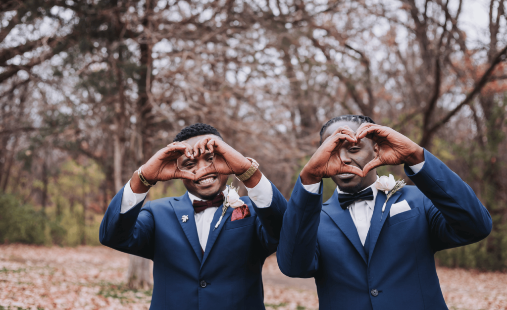 Image of groom and best man making hearts with their hands for the camera. 
