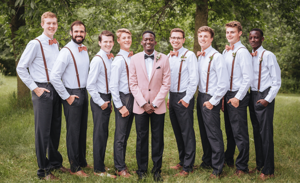 Image of 8 groomsmen lined up with groom in the middle. All men are smiling for wedding party photos. 