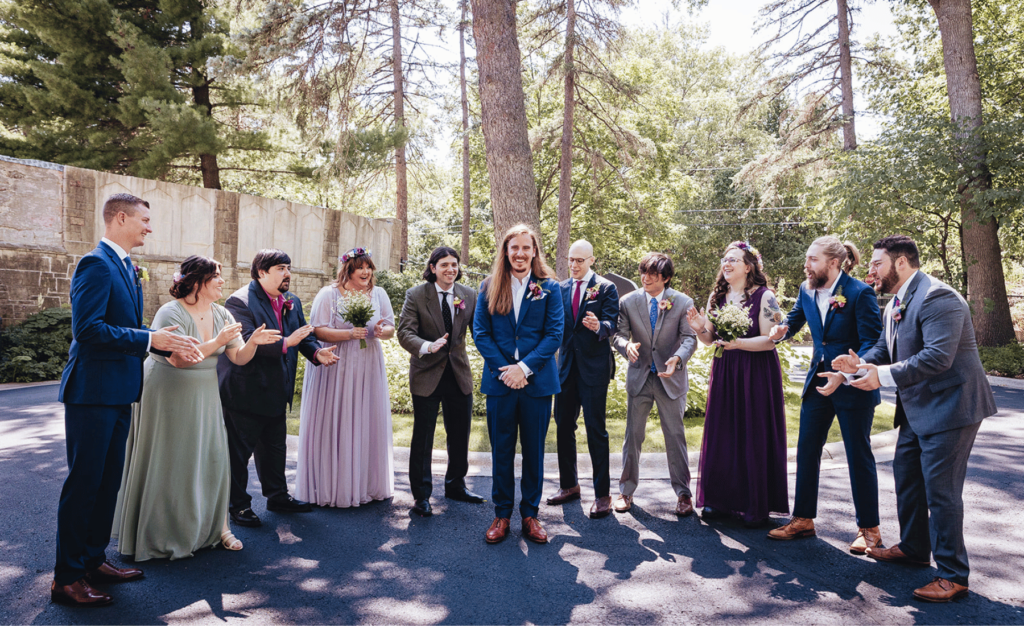 Image of a wedding party circling around a groom cheering and clapping for wedding party photos. 