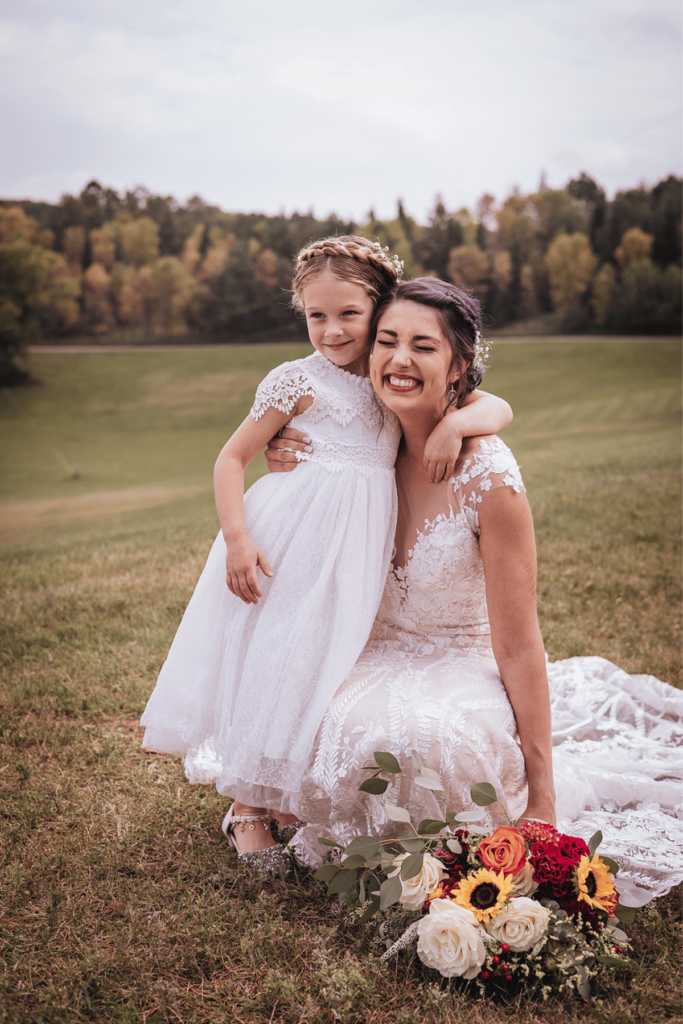 Image of a bride smiling with a small flower girl who is looking away from the camera. 