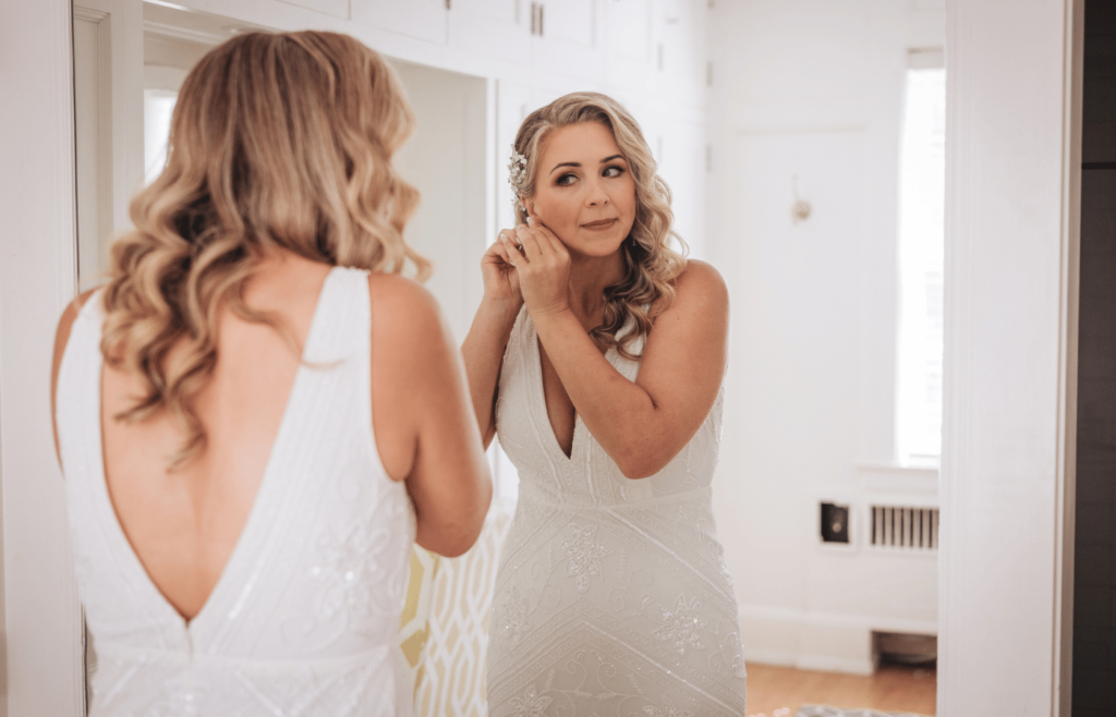 Image of a bride Getting ready photos wedding. She's putting on earrings in a mirror with her wedding dress on. 