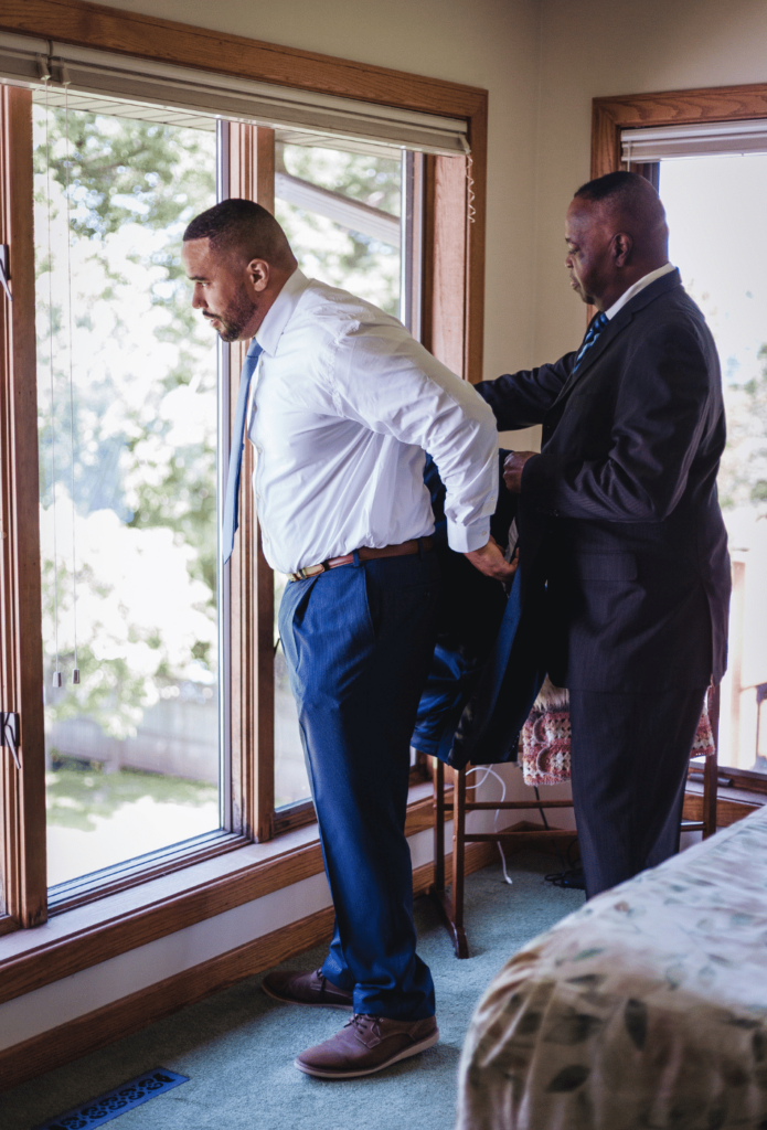 Image of a father helping a son into a groom suit. 