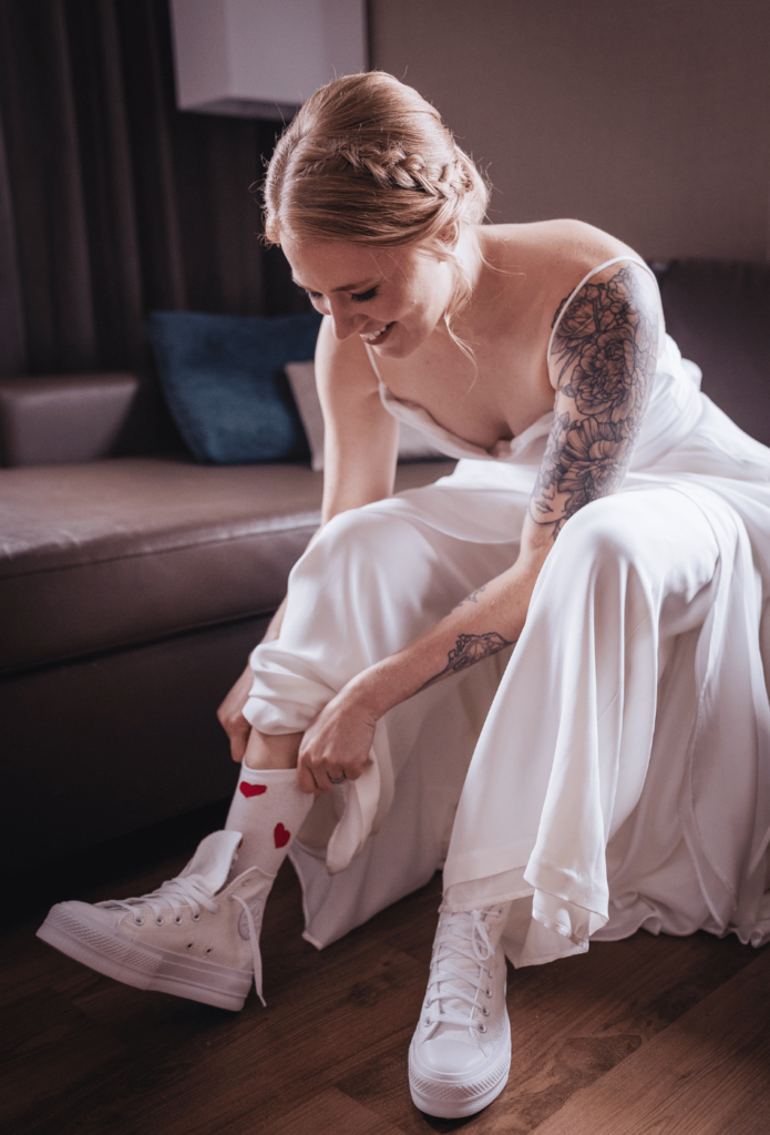 Image of a bride putting on socks with hearts and then sneakers on as she's getting ready photos wedding. 