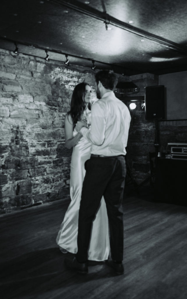 Image of a bride and groom sharing a first dance, the image is in black and white. 
