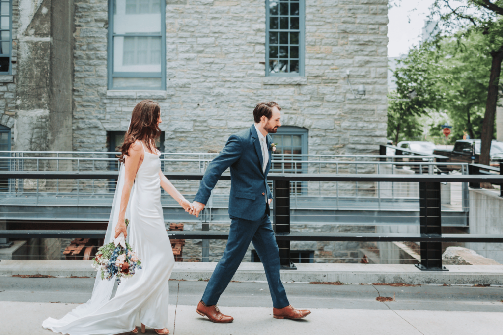 Image of a bride and groom walking together hand in hand outside. 
