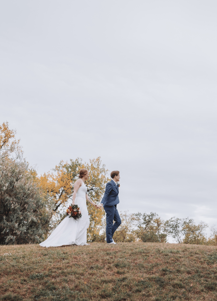 Image of a newly married couple walking hand in hand outside during fall. This is showing an image you can share on social media if you're wondering what to do with wedding photos.