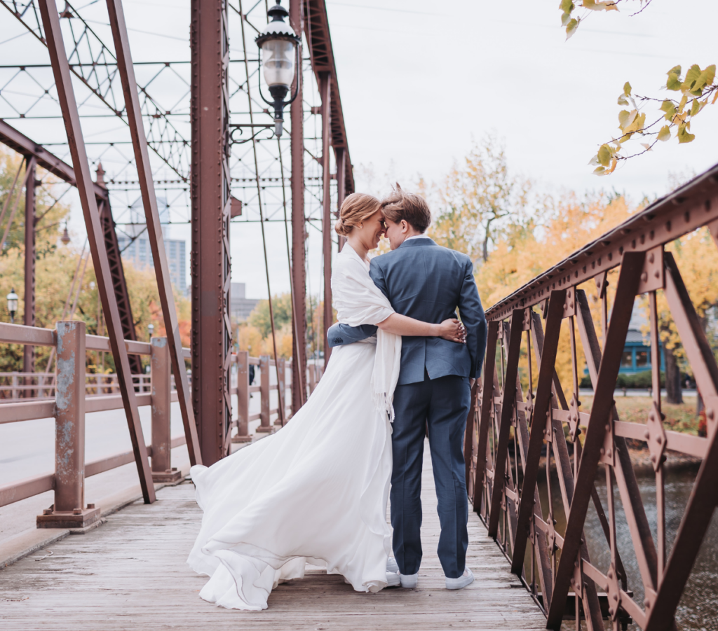 Image of a couple standing outside on a bridge looking at each other lovingly. 