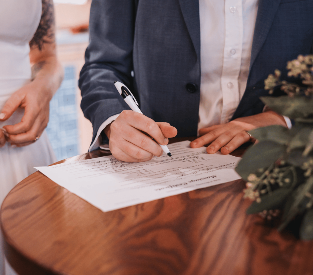 Image of a wedding couple signing their marriage certificate. 
