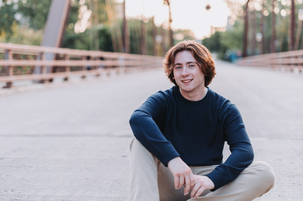Minneapolis senior photo idea: senior guy sits on Minneapolis bridge