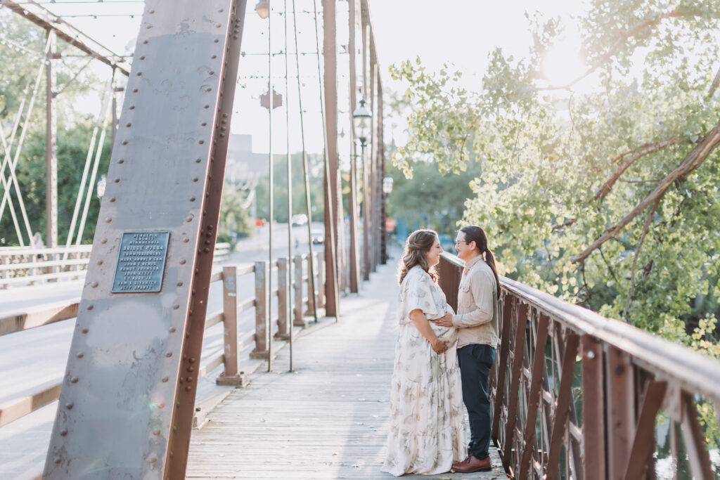Pregnant woman and parter stand on a bridge in Minneapolis during their maternity photoshoot