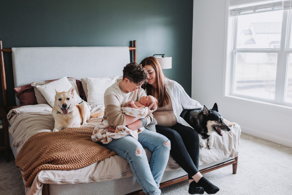 Couple in their home on their bed with two dogs holding their newborn during their newborn photo session