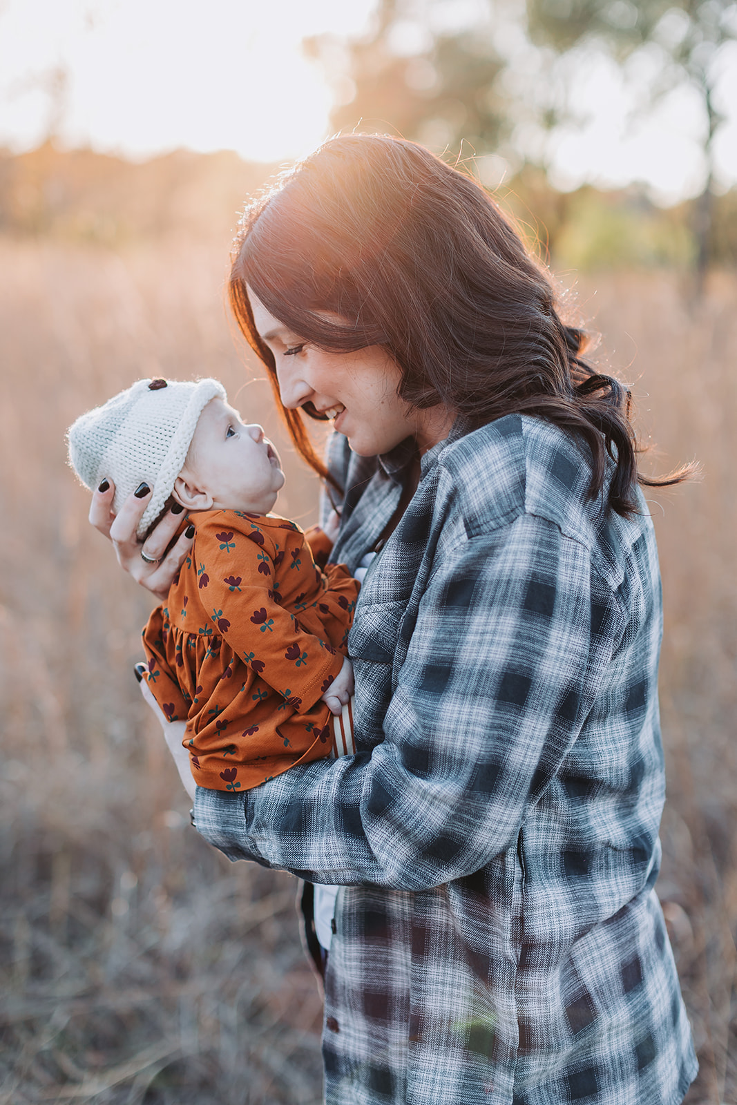 Mom and baby in a field with the sun setting behind them during their Minneapolis newborn photography session